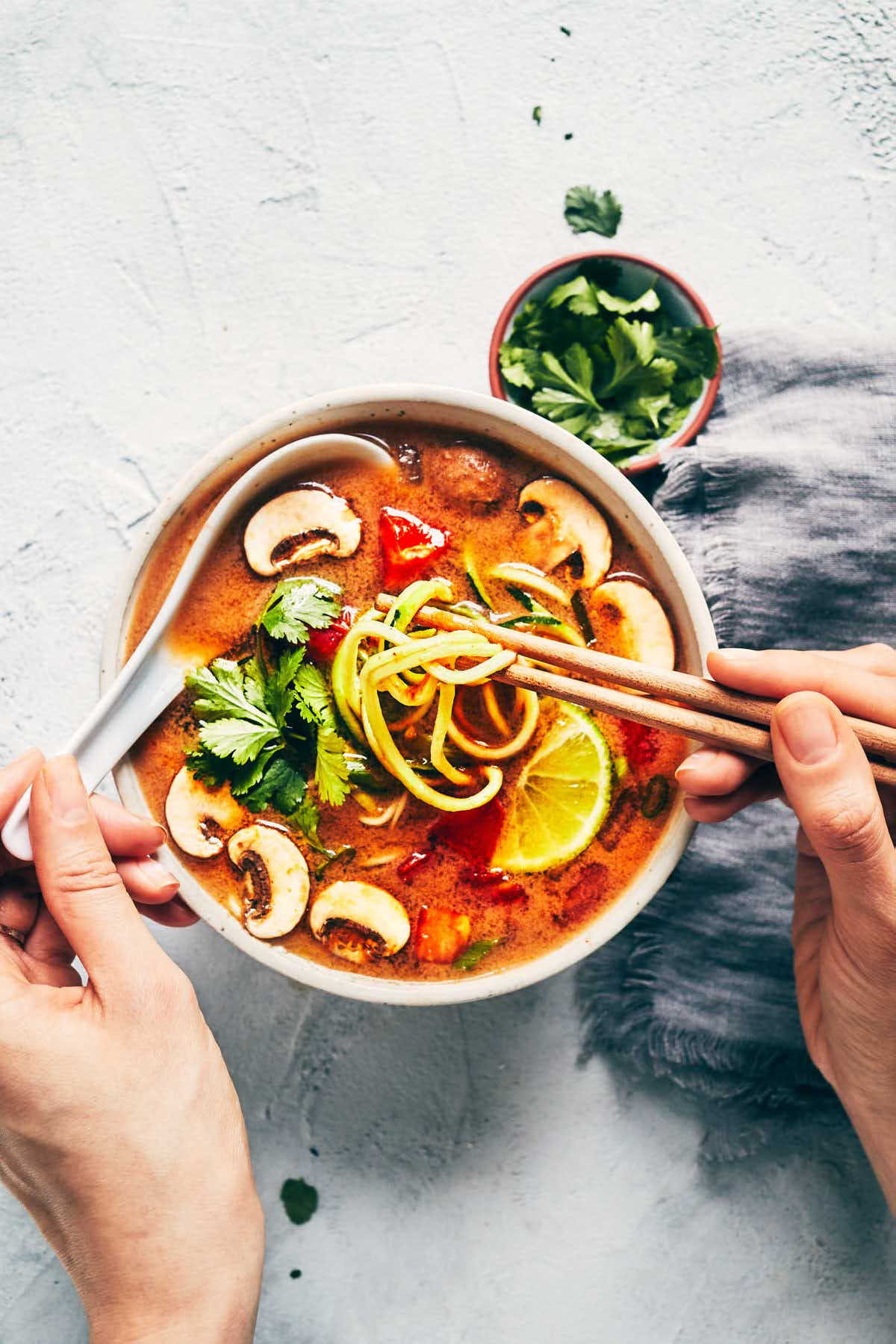 Hands digging into vegan tom yum soup with chopsticks and spoon