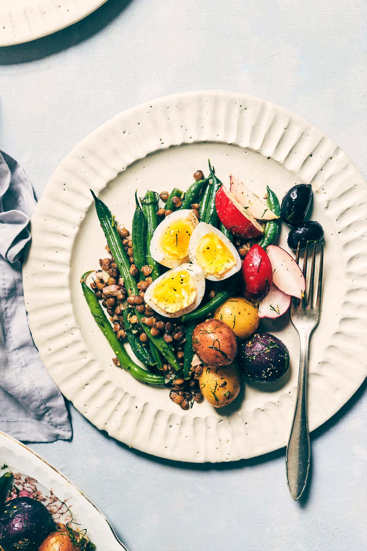 Plate of nicoise salad with egg, green beans and black olives