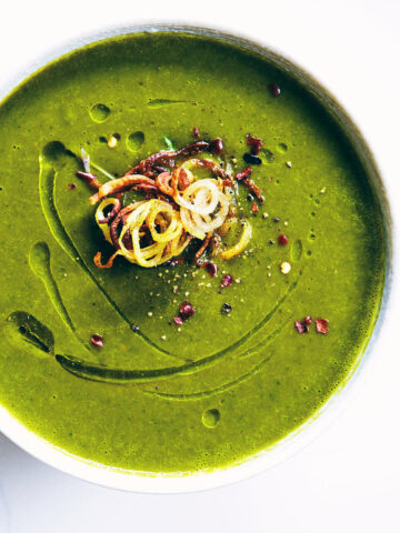 Close up of watercress soup on a white counter topped with crispy shoestring potatoes