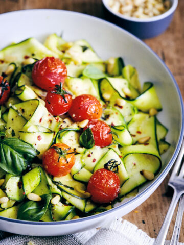 Zucchini papperdelle with roasted tomatoes and basil in a bowl with pine nuts on the side
