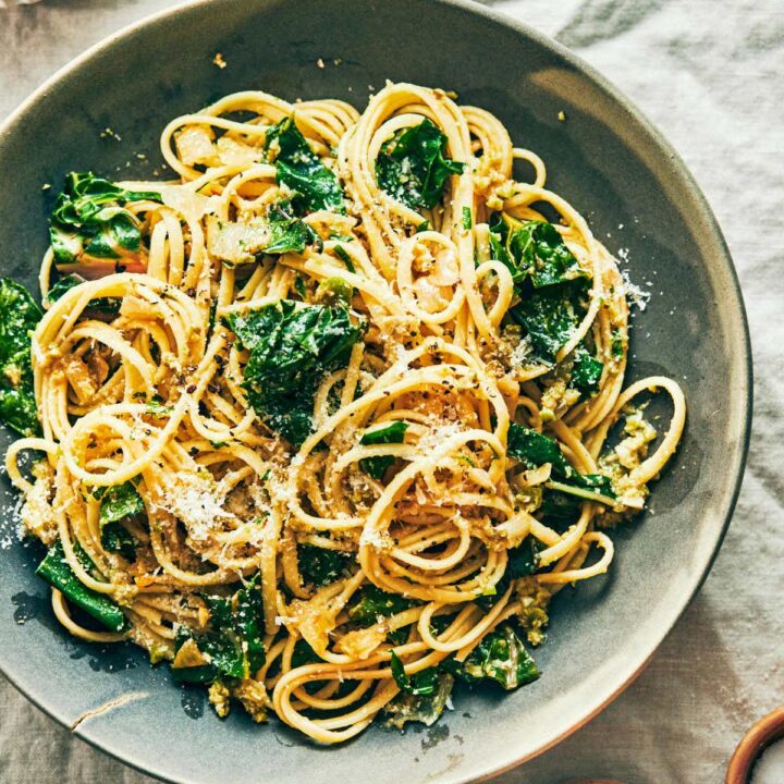 Lemon swiss chard pasta served on a blue plate with lemon and pepper peeking in