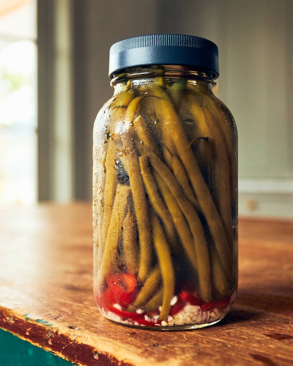 Jar of quick pickled green beans sitting on a wooden table in a kitchen