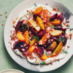 Labneh topped with roasted beets and fresh herbs on a light green table