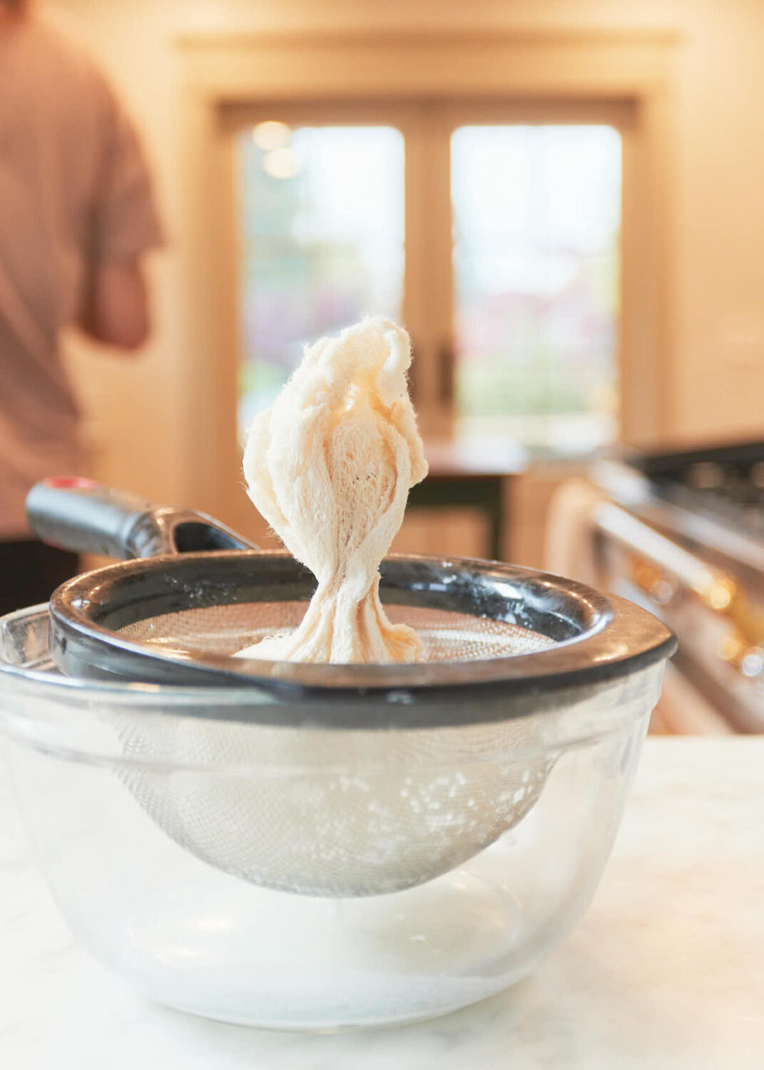 Yogurt sitting in a cheesecloth lined sieve on the counter, draining to make labneh