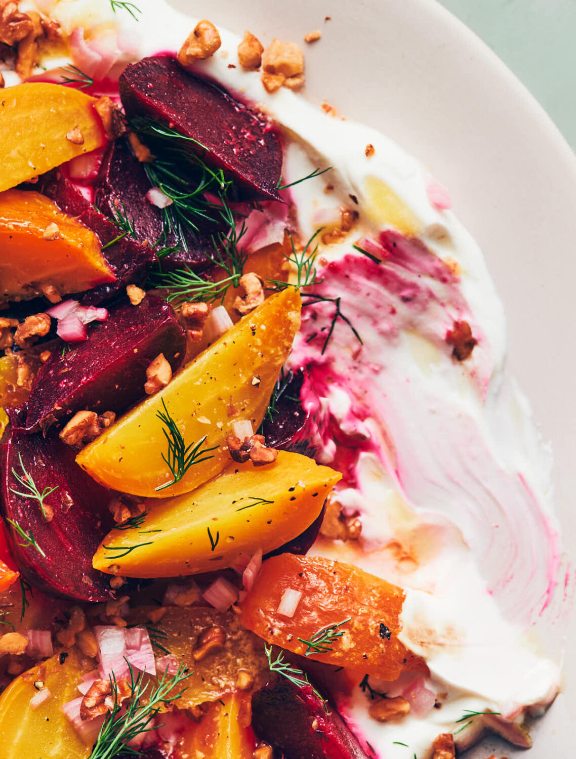 Close up of roasted red and yellow beets on top of labneh, garnished with dill, walnuts and shallots
