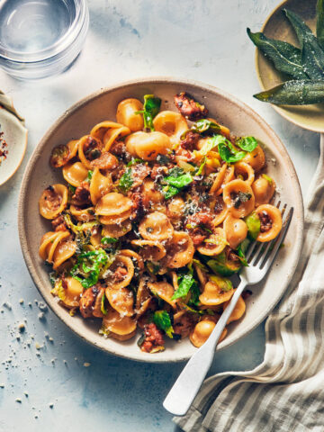 Bowl of spicy sausage and brussels sprout pasta with crispy sage on the side and a fork digging in