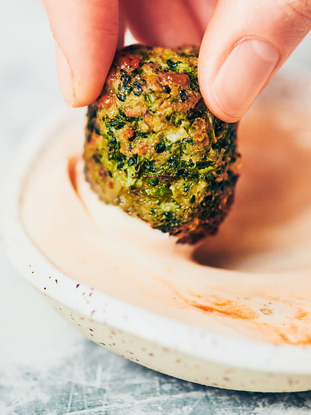 A close up of hand holding a brocolli tot being dipped into creamy buffalo sauce