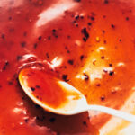 A close up of shiny homemade Thai sweet chili sauce with a white spoon stirring it