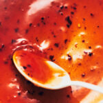 Close up photo of a white spoon stirring Thai sweet chili sauce