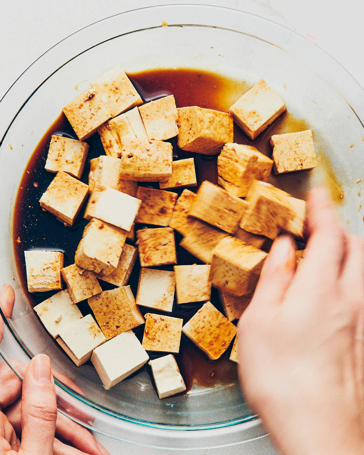A hand tossing cubed tofu and tamari until the tofu is well coated