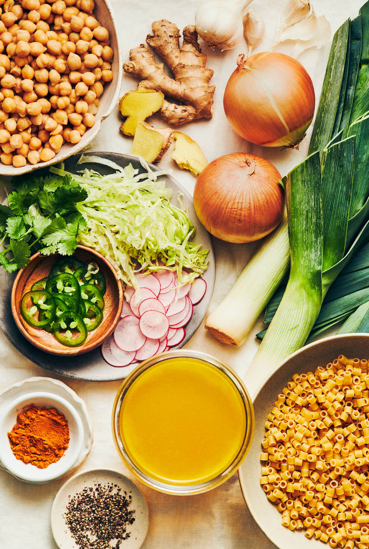 The ingredients to make vegan golden chickpea noodle soup: leeks, yellow onions, vegetable broth, chickpeas, pasta, ginger, turmeric, and black pepper