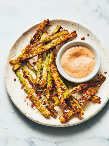 Plate of air fryer broccoli fries and vegan dijon aioli sitting on a marble counter