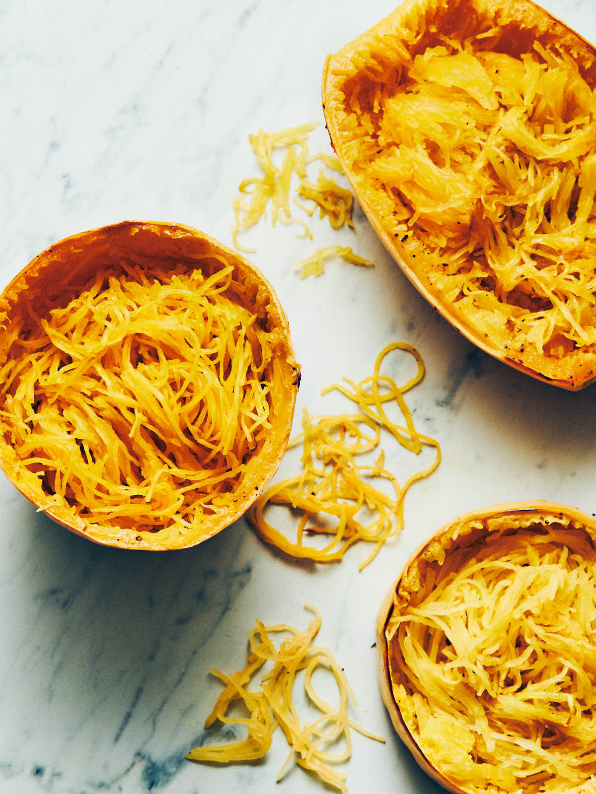 Spaghetti squash cooked three ways with noodles scooped out sitting on a marble surface