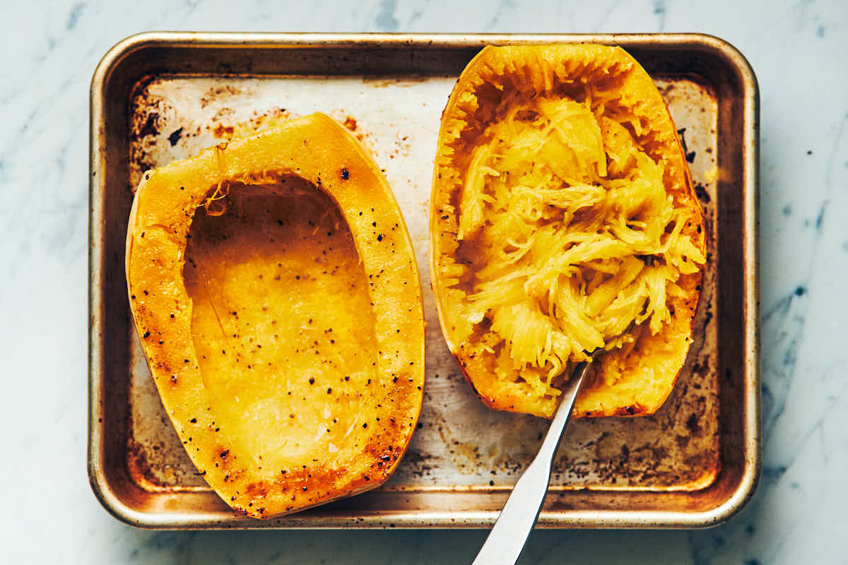 Spaghetti squash cut in half lengthwise and cooked on a metal baking sheet with noodles scooped out