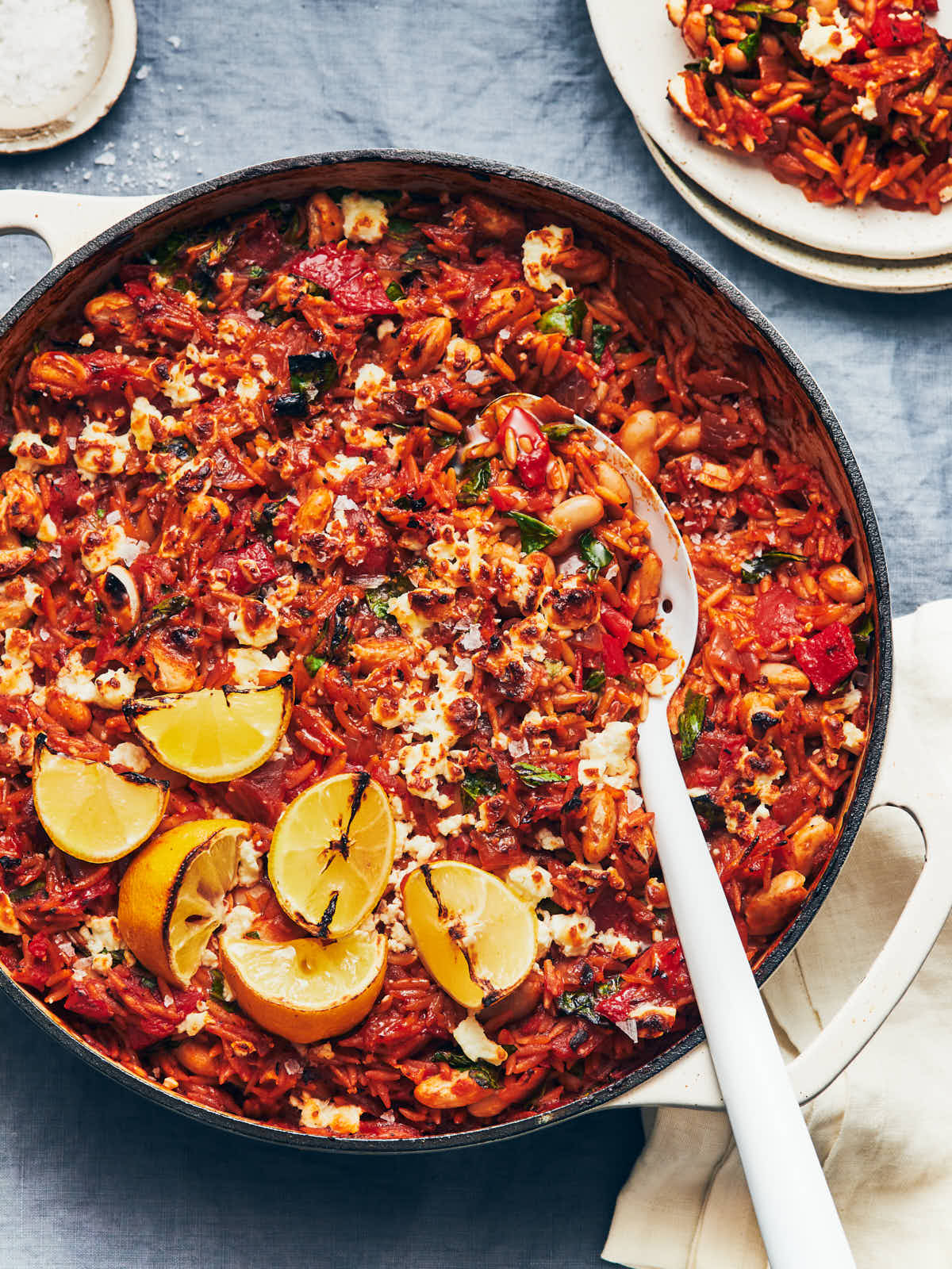 An overhead of one pot tomato harissa orzo with broiled lemons and a white enamel serving spoon