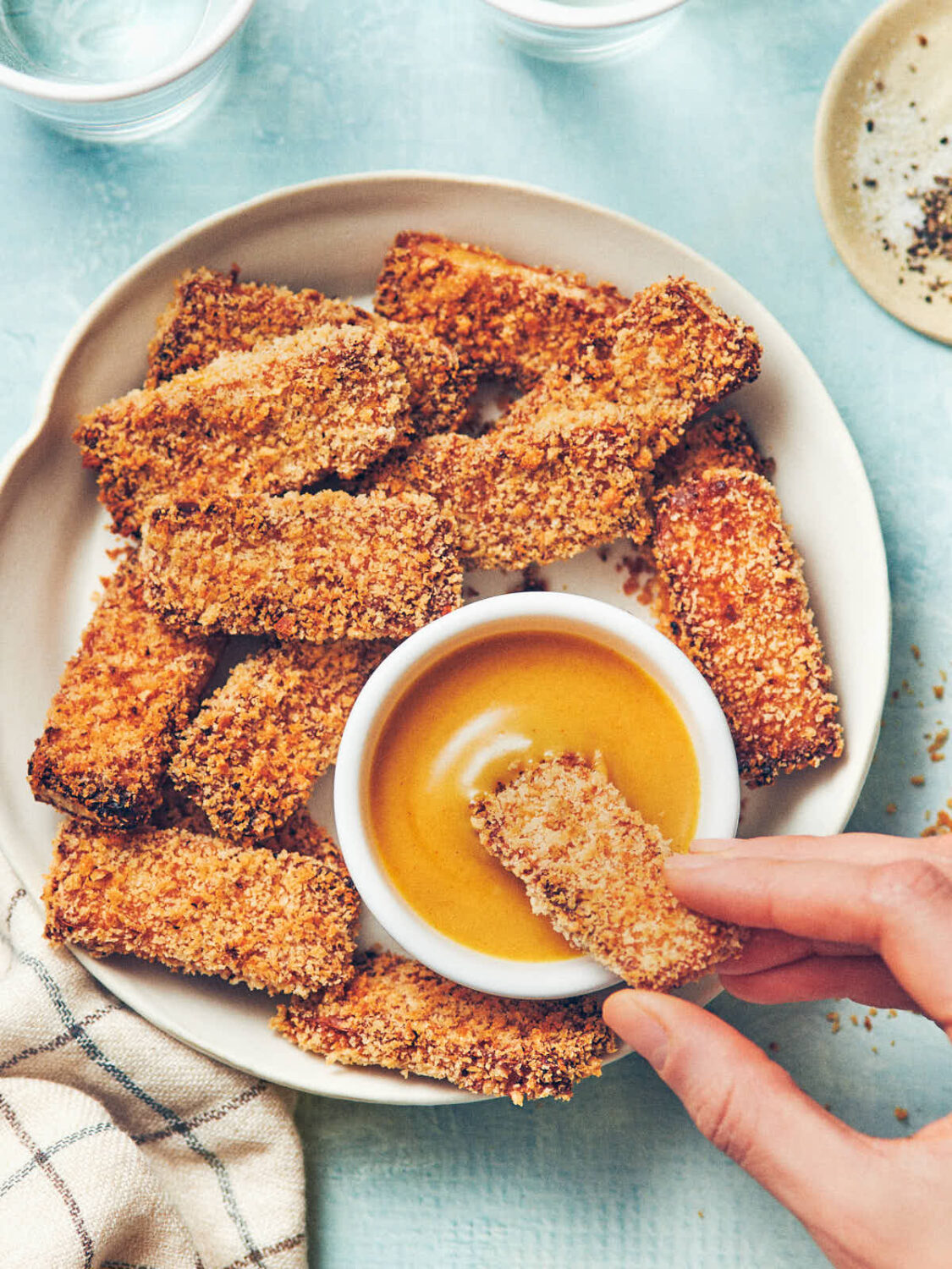 A plate of crispy air fryer tofu, with a crispy tofu stick being dipped into homemade honey mustard sauce. 