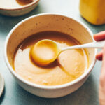 A bowl of homemade honey mustard sauce in a bowl with a spoon scooping out some sauce.