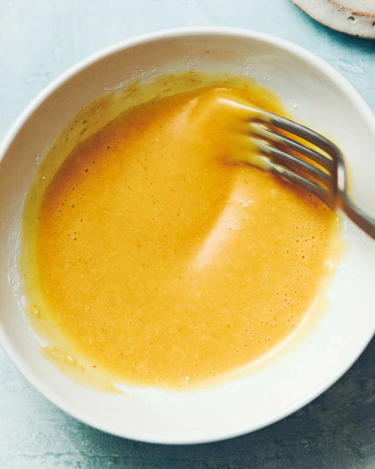 A fork mixing homemade honey mustard sauce in a white bowl.