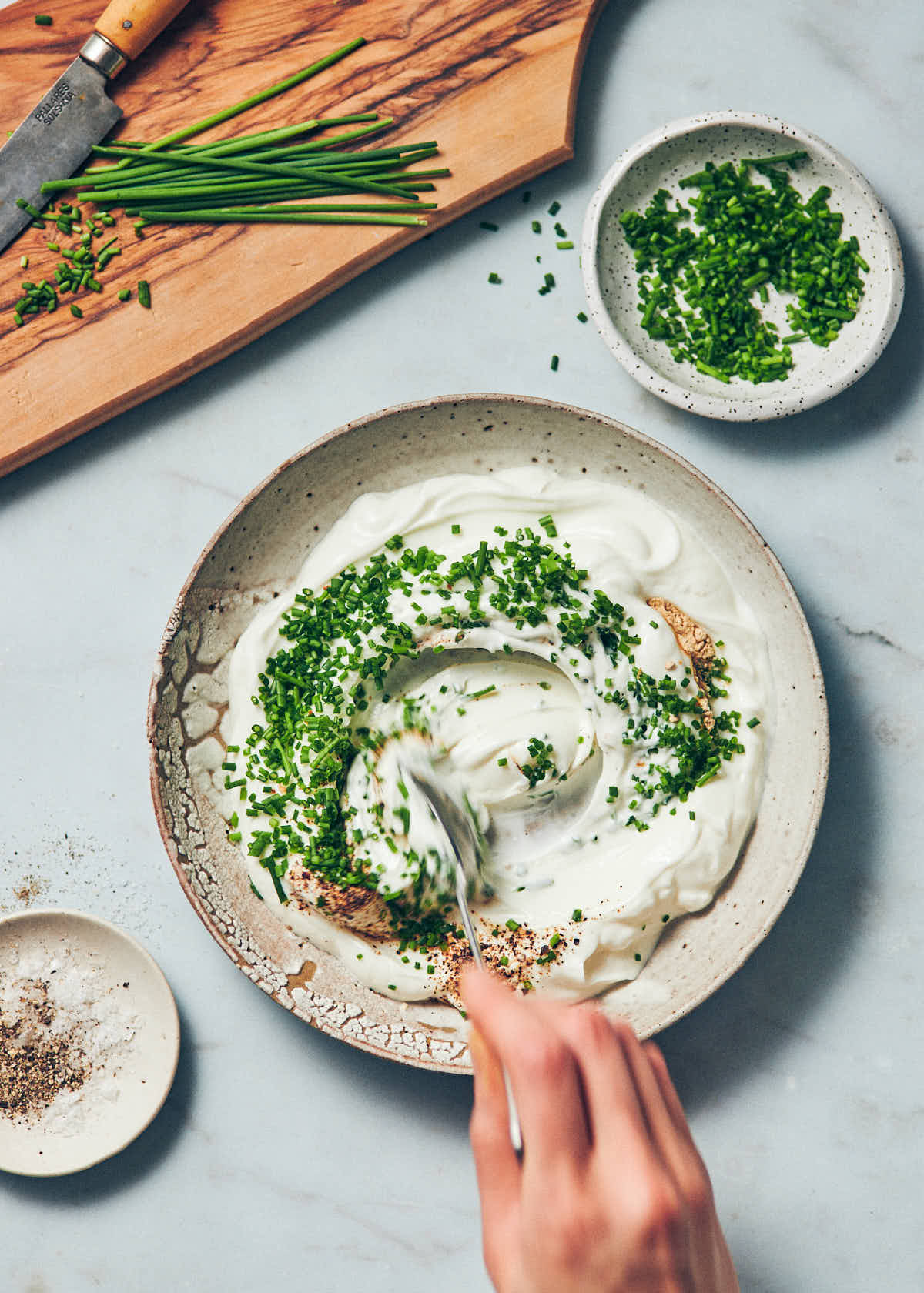 A bowl of Greek yogurt with fresh chopped chives being stirred in with a spoon.