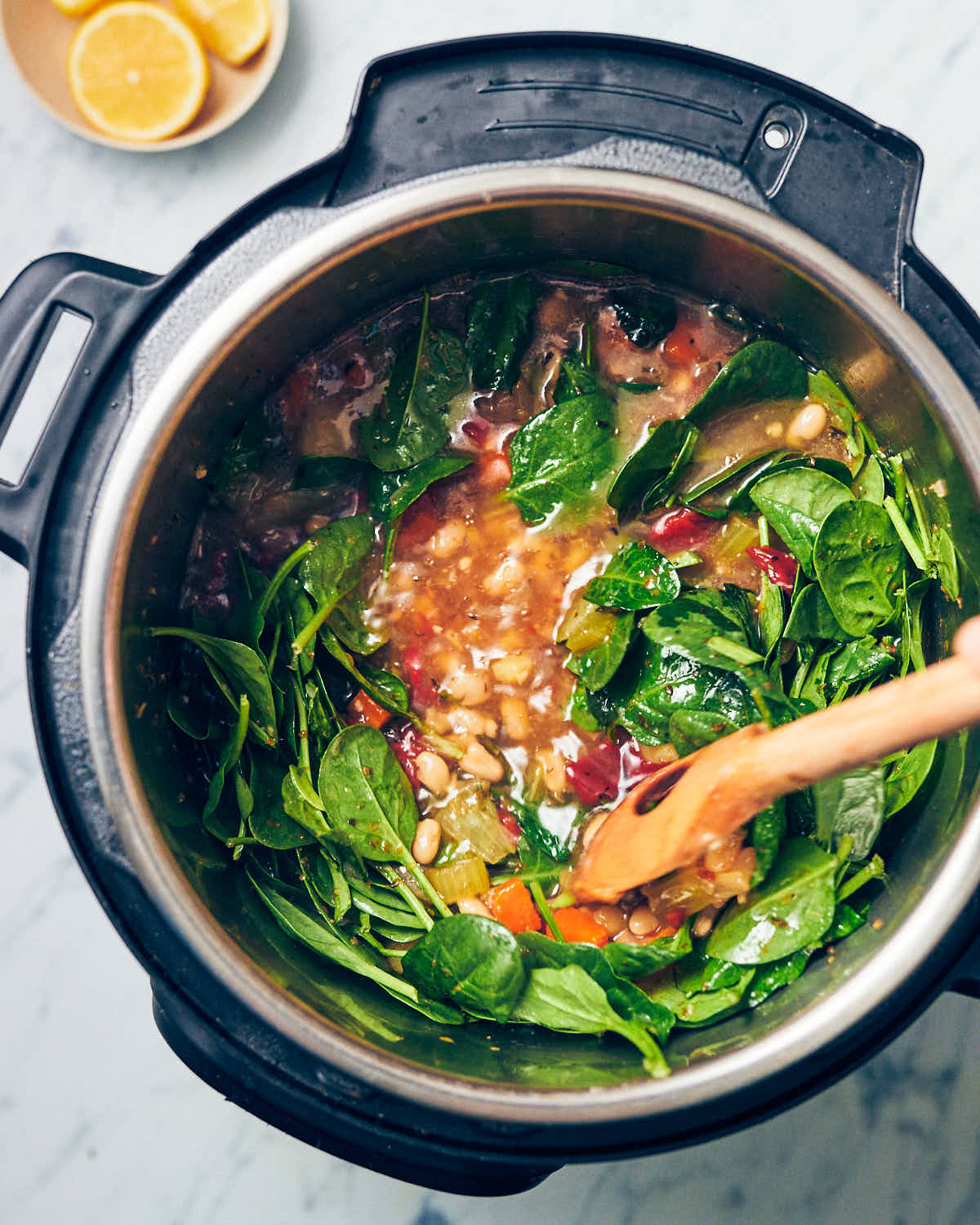 A wooden spoon stirring baby spinach into an Instant Pot full of navy bean soup