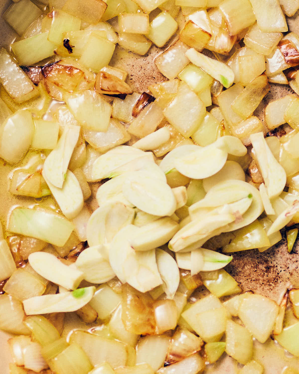 A pan of diced onions cooked until pale golden, with fresh sliced garlic cloves