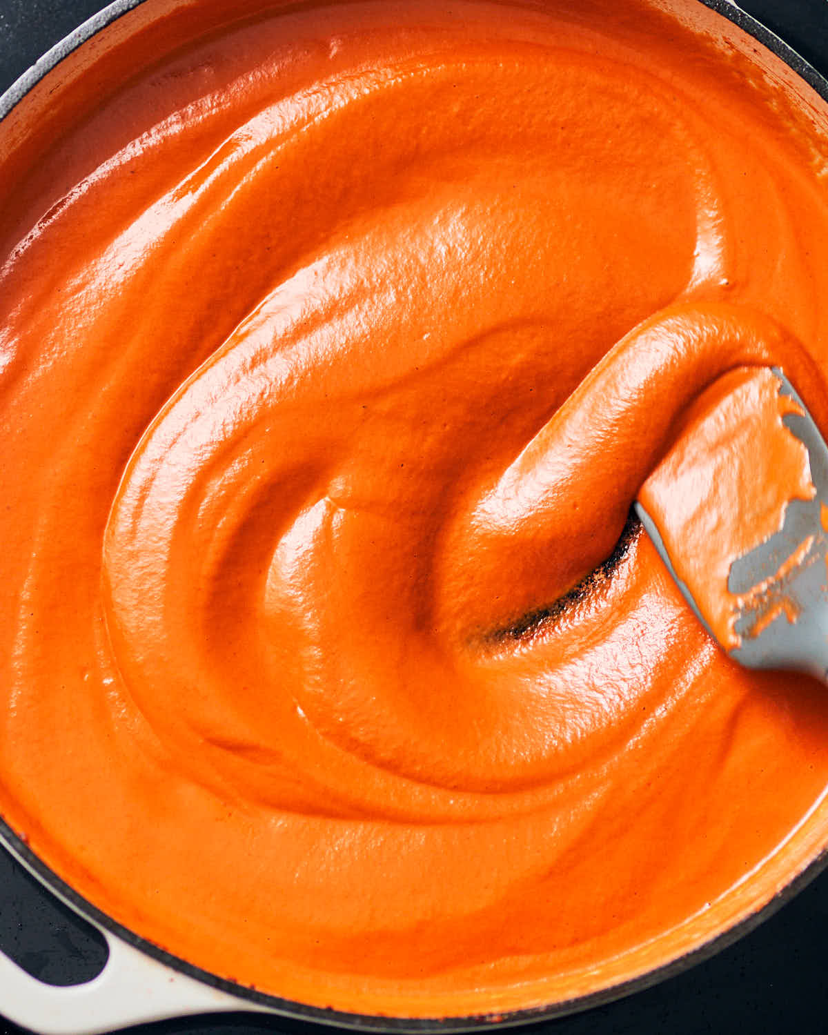 Creamy vegan vodka sauce in a pan, being stirred with a spoon