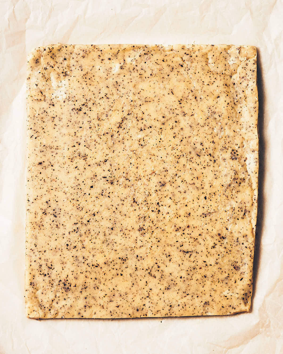 Earl grey shortbread dough that has been rolled into a square on parchment paper.