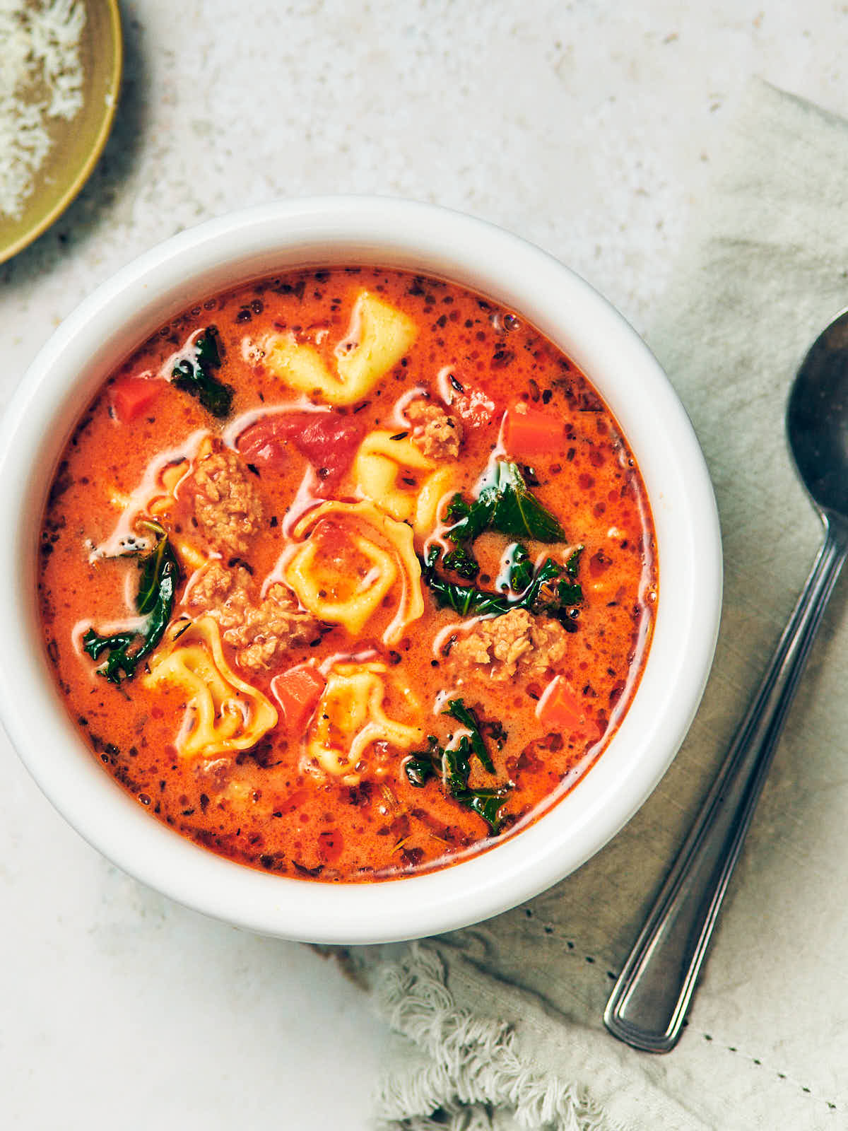 A bowl of creamy vegetarian tortellini soup with kale and plant based sausage.