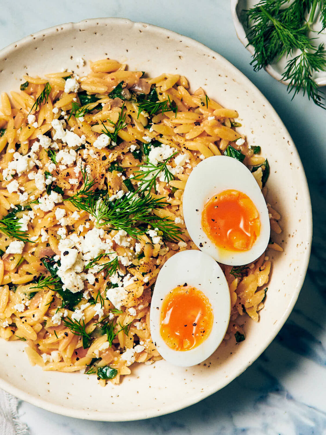 A single serving of Lemon Spinach Orzo, topped with a soft boiled egg halves.