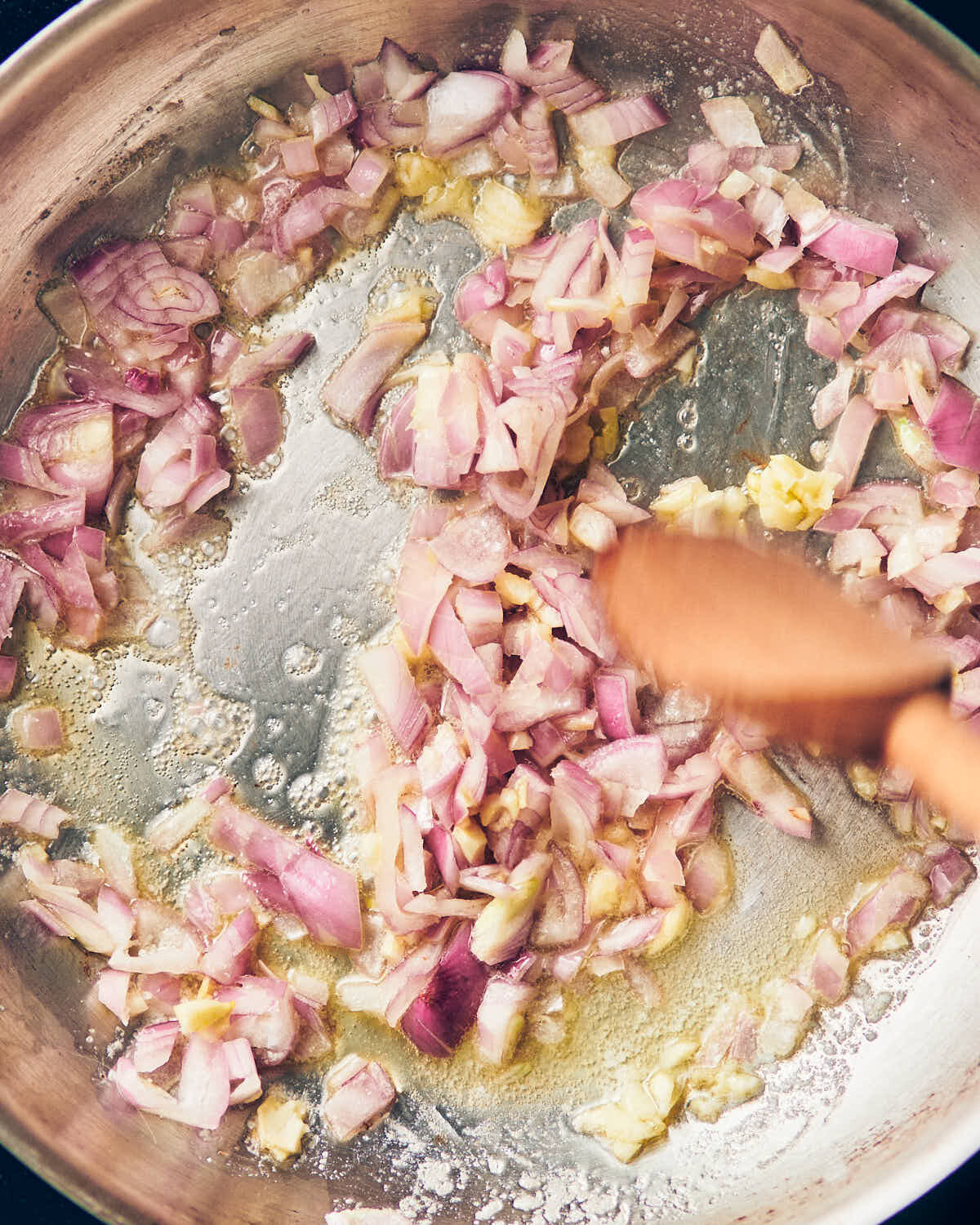 Shallots and garlic being sauteed in a skillet with olive oil.