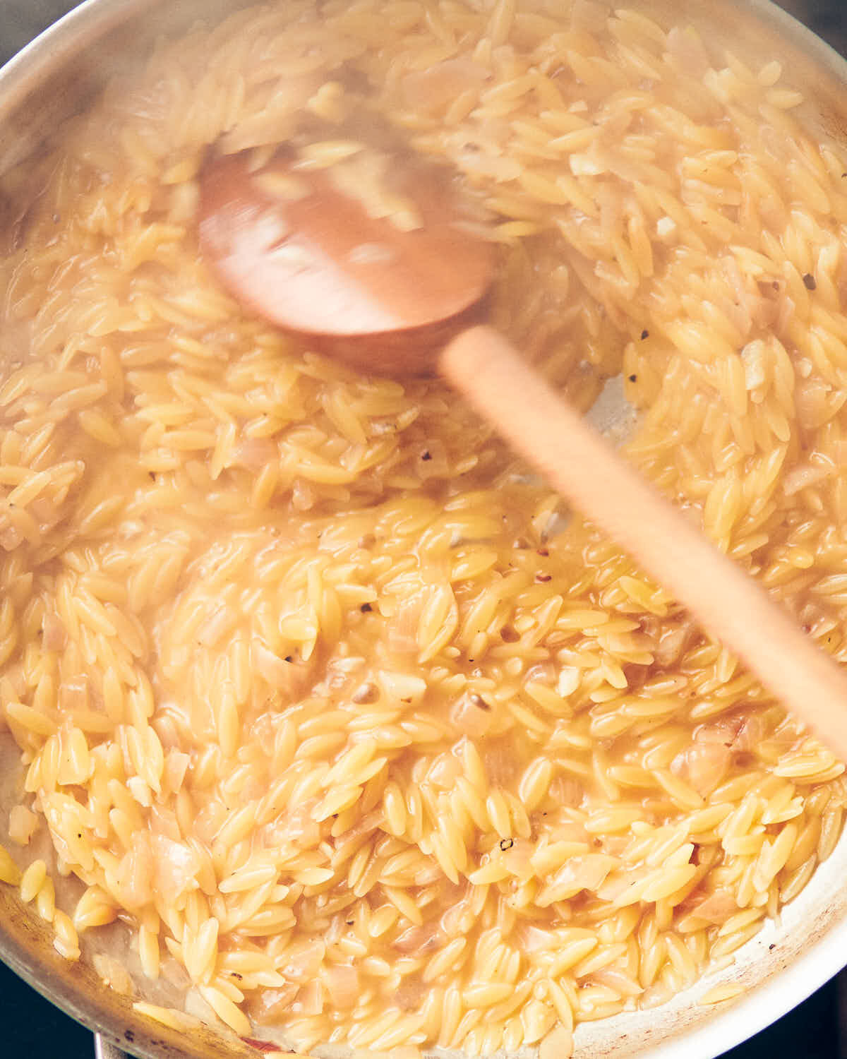 Partially cooked orzo being stirred with a wooden spoon.