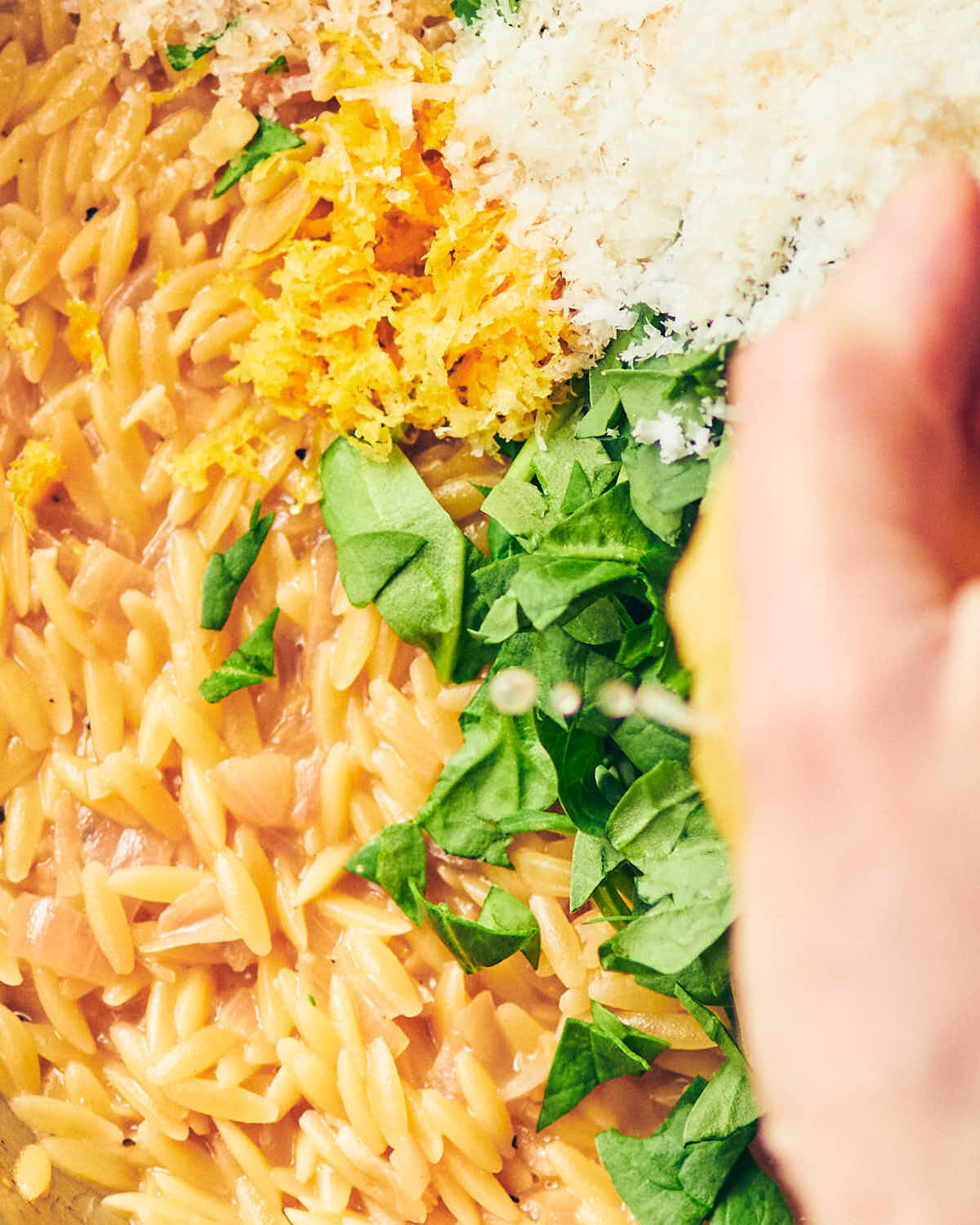 Orzo cooked al dente, being topped with lemon zest, parmesan, spinach and fresh lemon juice.
