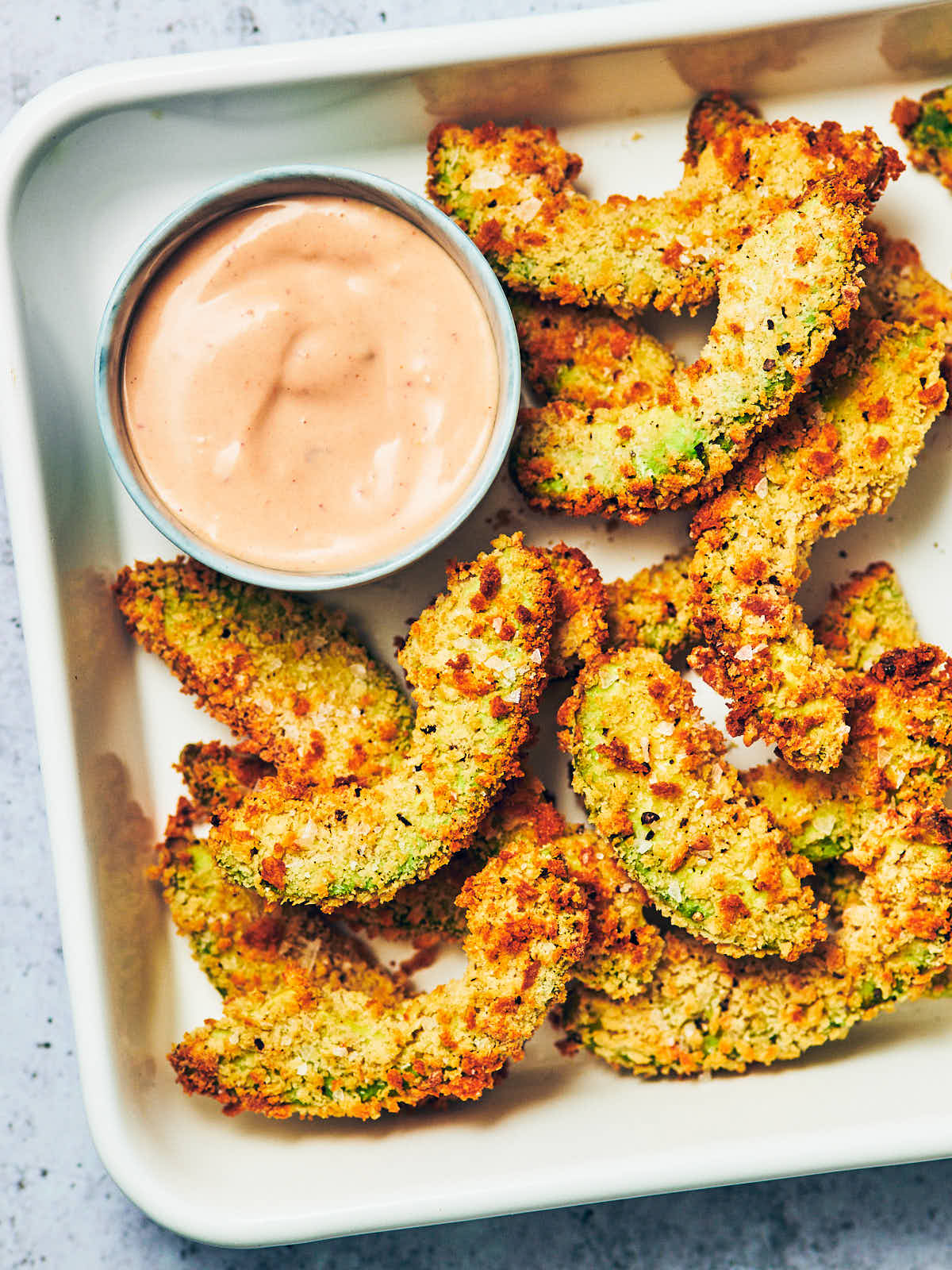 Crispy vegan avocado fries in a serving dish with a bowl of vegan chipotle mayo.