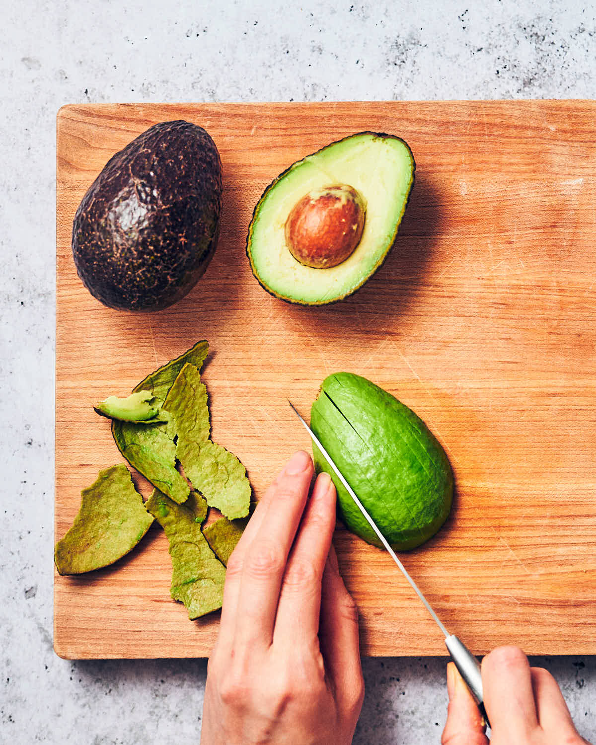 Avocado being sliced with a knife on a wooden cutting board