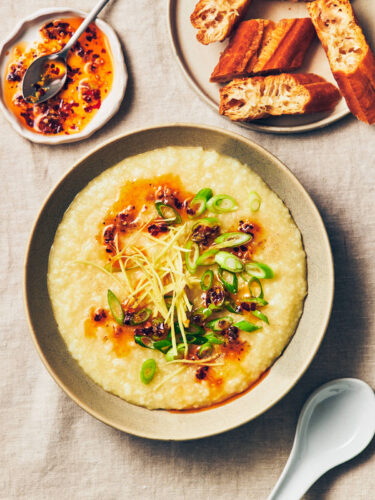 A bowl of vegan congee (rice porridge) topped with chili garlic oil, scallions, ginger, and white pepper on a table