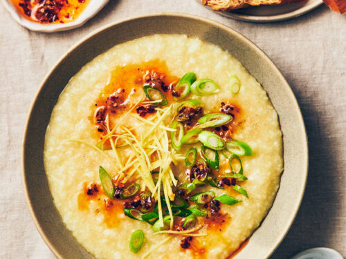 A bowl of vegan congee (rice porridge) topped with chili garlic oil, scallions, ginger, and white pepper on a table