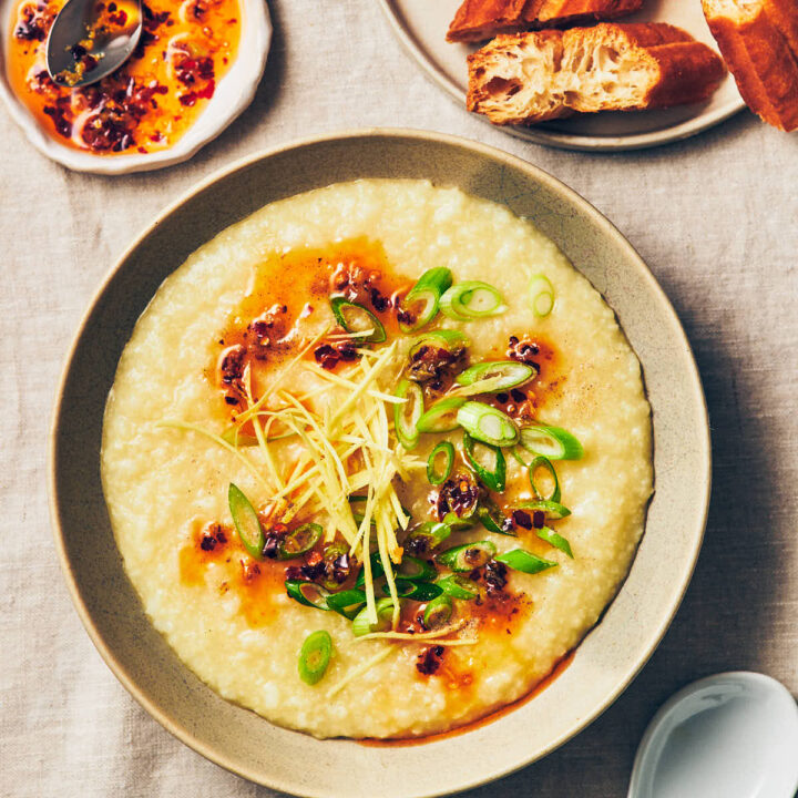 A bowl of vegan congee (rice porridge) topped with chili garlic oil, scallions, ginger, and white pepper on a table