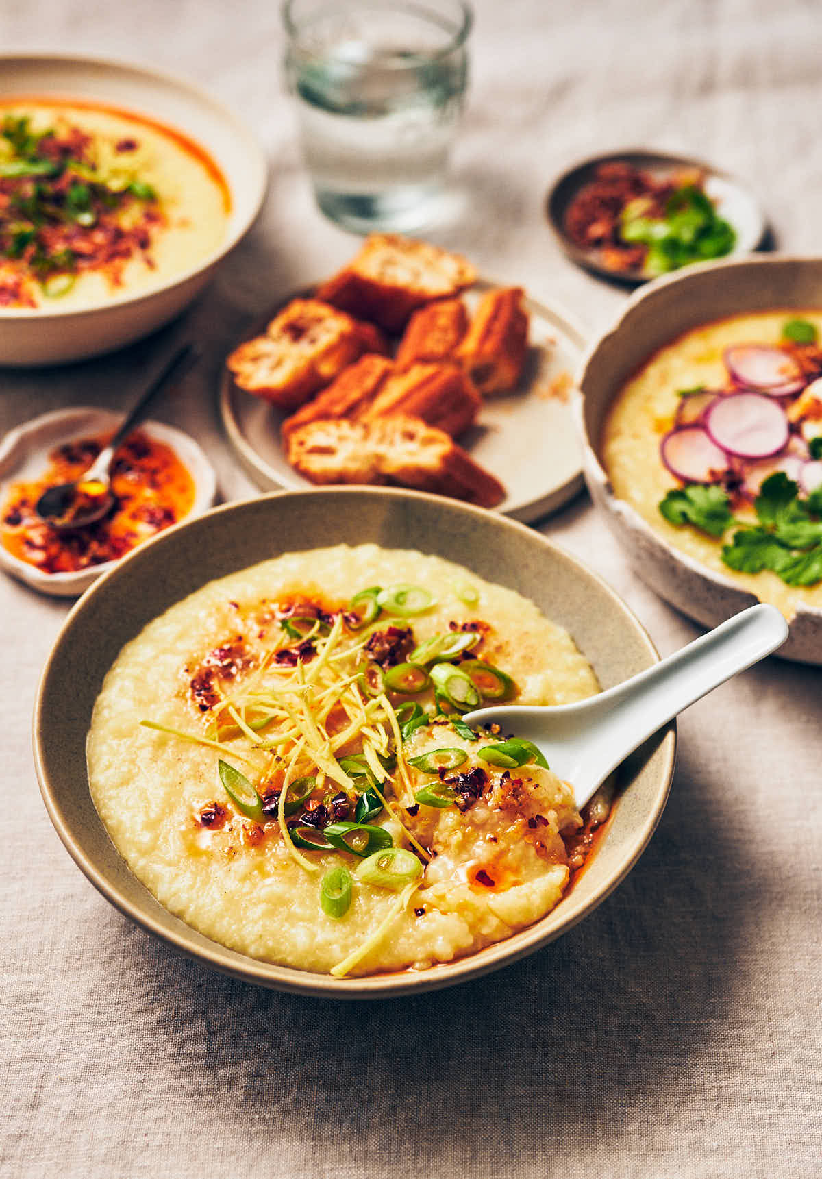 A bowl of vegan congee topped with chili garlic oil and scallions, with a white Chinese spoon scooping out some congee.