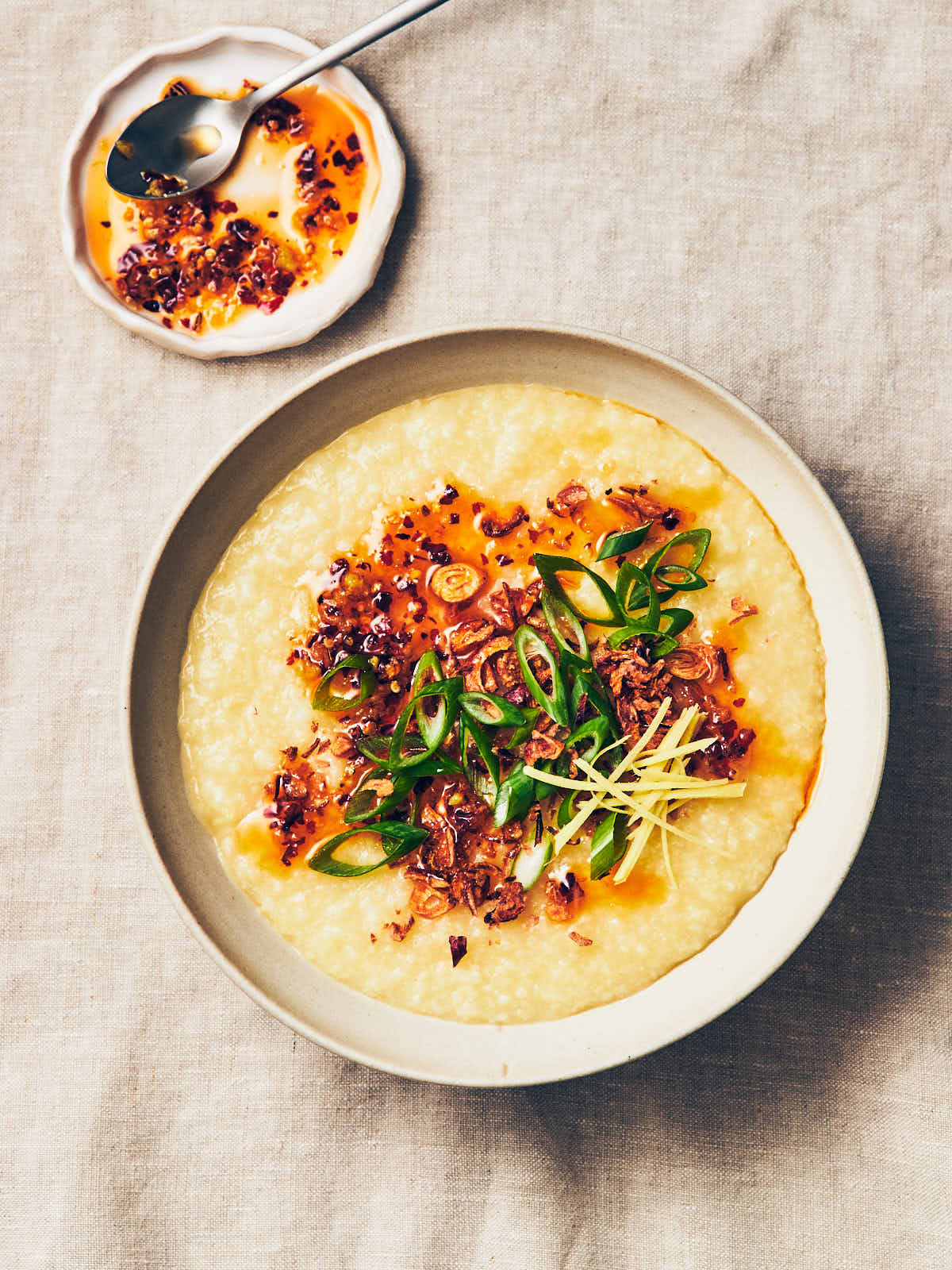 A bowl of vegan congee with homemade chili garlic oil, crispy shallots, scallions, and ginger on top.