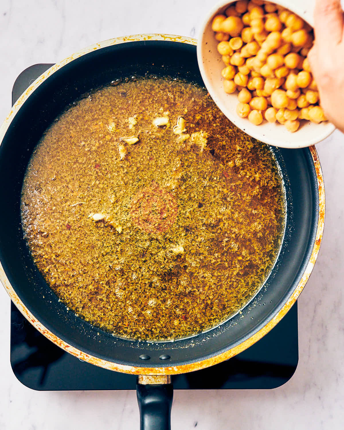 A skillet with oil, spices, and garlic with chickpeas being added.