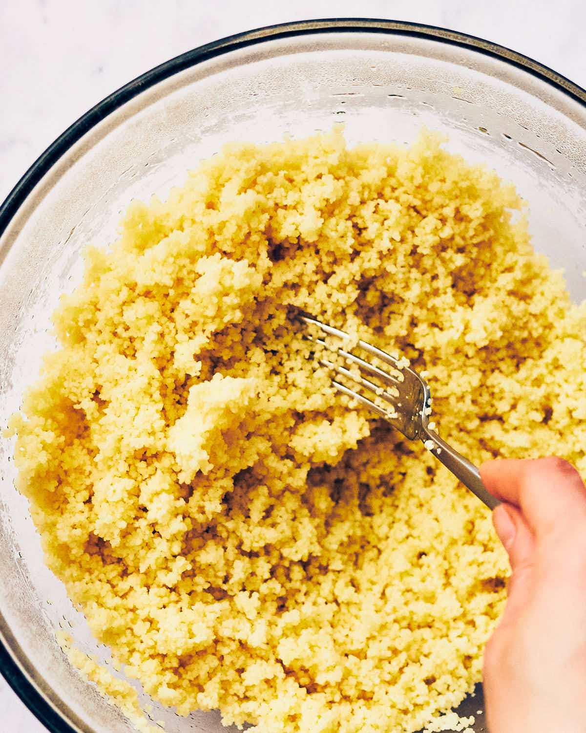 A fork fluffy steamed couscous in a bowl for Halloumi Couscous Salad with Lemon.