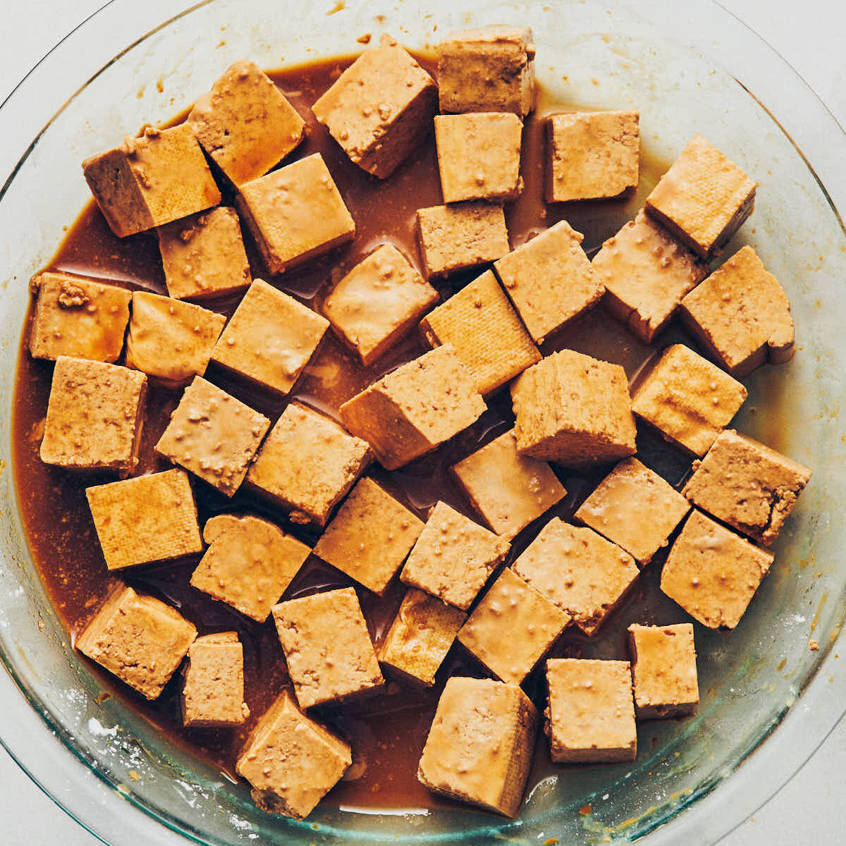 Cubed tofu sitting in a shallow glass dish of tamari to marinate
