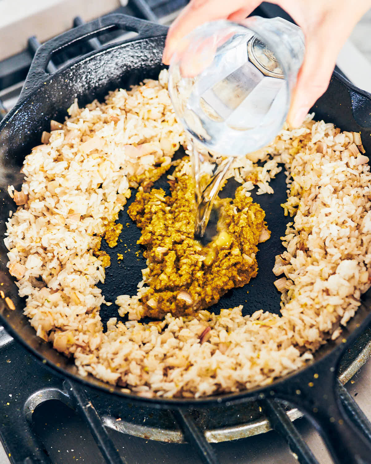 Green curry paste and water being cooked in a skillet with vegan fried rice.