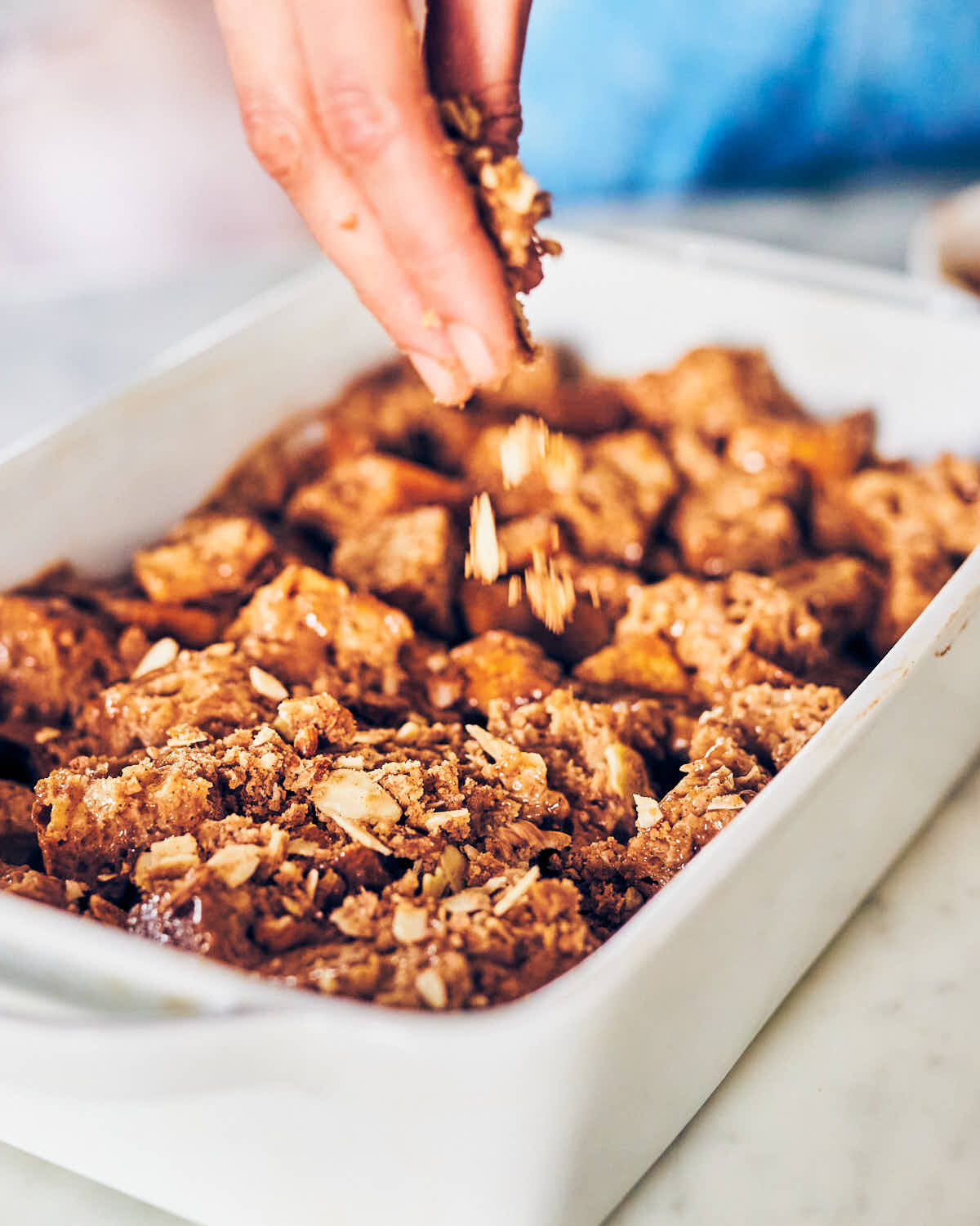 Sprinkling an almond cinnamon crumble over french toast casserole before baking.
