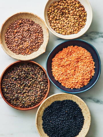 Different examples of lentils in bowls: red, green, brown, French, and black lentils.