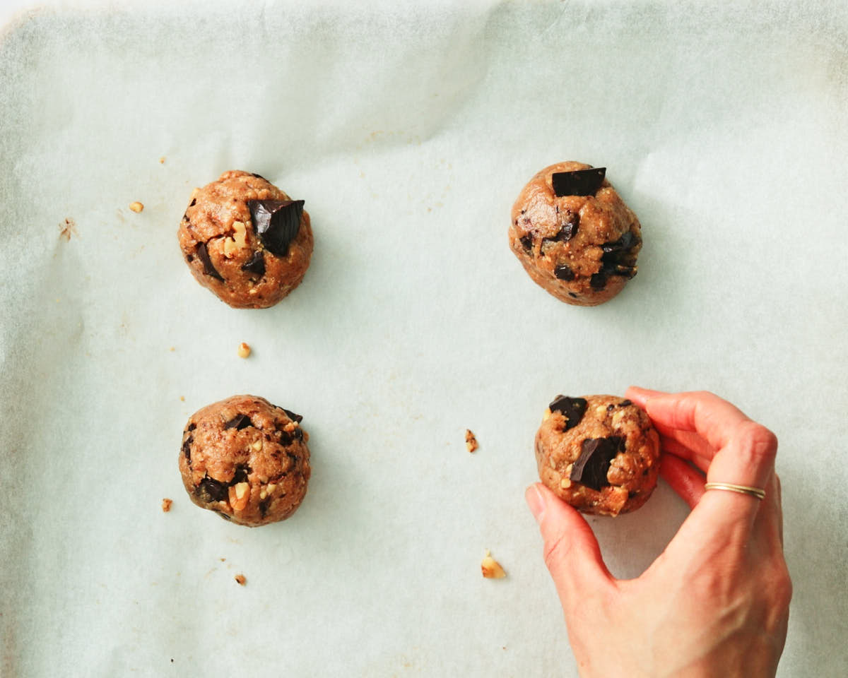 Placing balls of oat chocolate chip cookie dough out onto a parchment lined baking sheet.