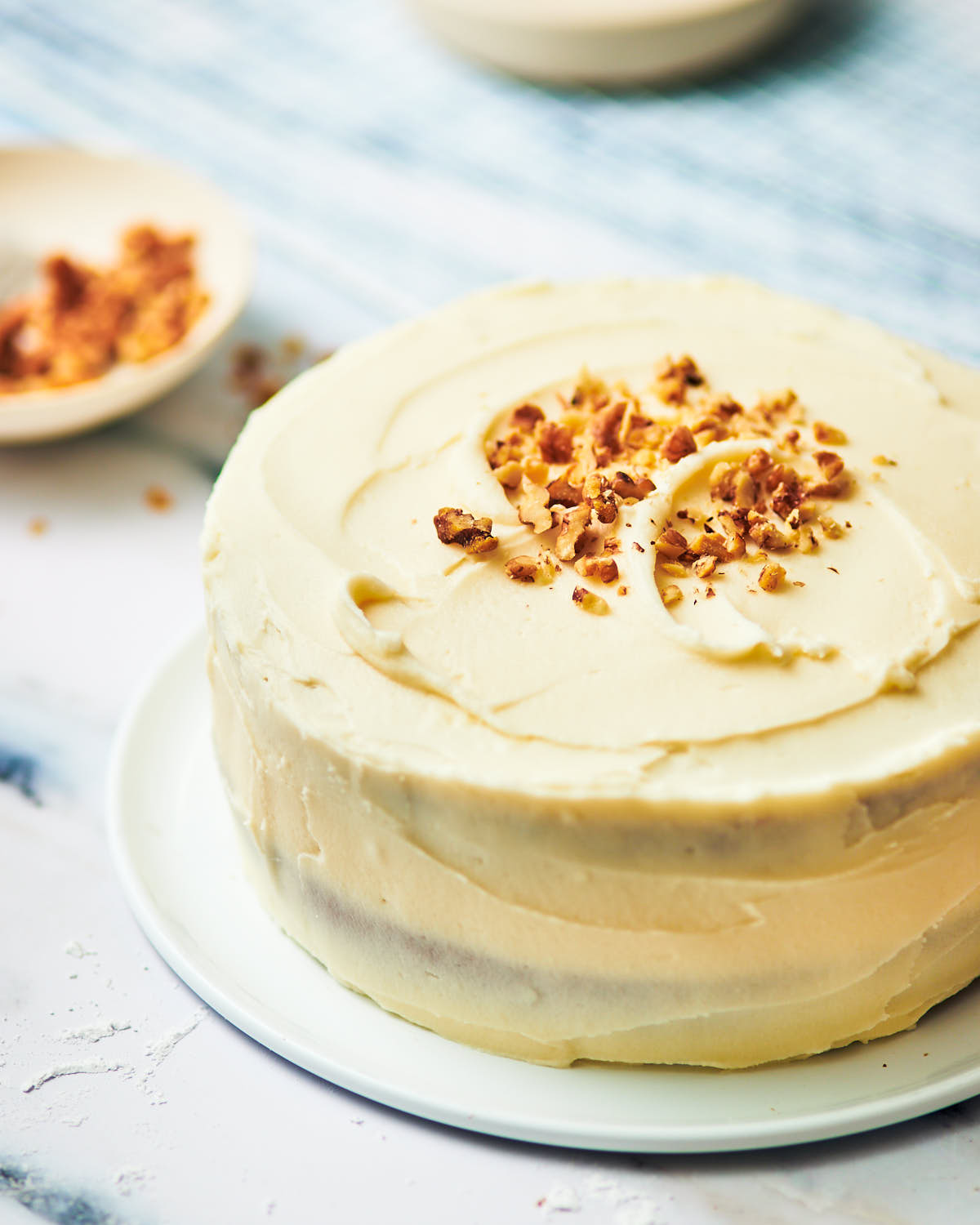 Banana walnut cake decorated with cream cheese frosting and chopped nuts.
