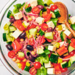 Greek cucumber salad with tomatoes, feta, peppers and olives in a bowl.