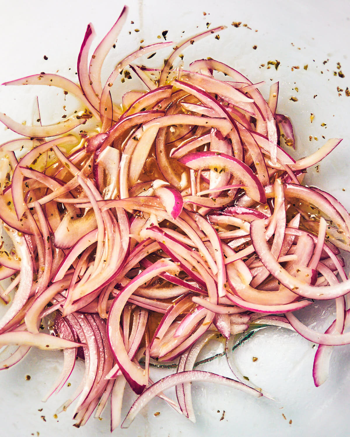 Thinly sliced red onions in a glass bowl of red wine vinegar for Greek Cucumber Salad.