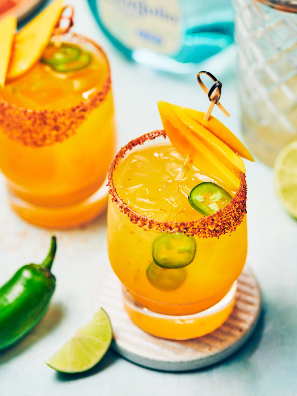 Two cocktail glasses of Spicy Mango Jalapeno Margaritas topped with fresh mango slices.